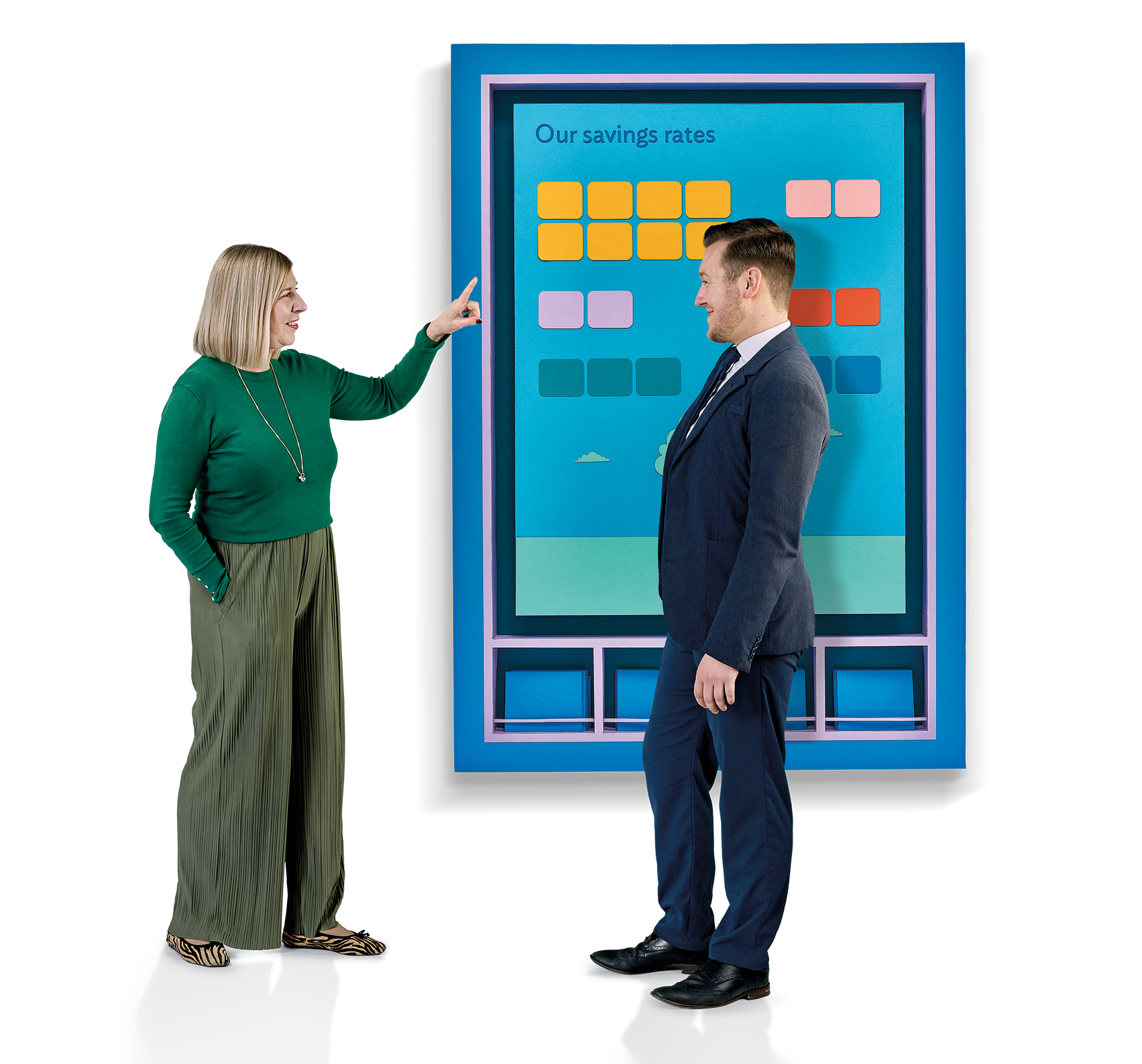 A man stood infront of a large media screen talking to a woman who is pointing at it