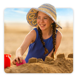close up image of a girl wearing a big sunhat and blue costume sat on the beach